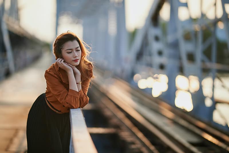 pensive woman standing near rails leaning on the fence