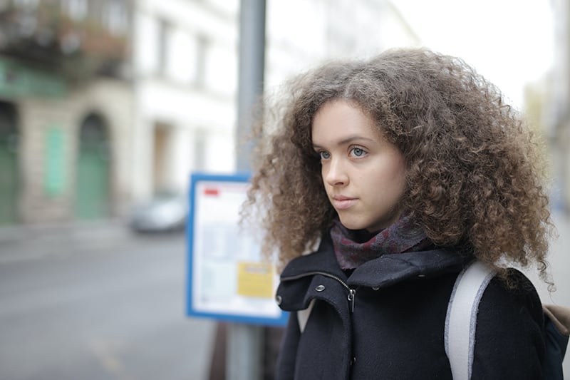 mulher pensativa, parada na rua e a olhar para o lado