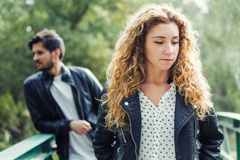 pensive woman walking in front of her boyfriend in the park