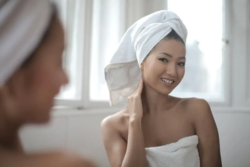 positive woman looking herself in the mirror with towel on her head