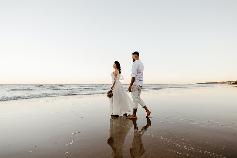 romantici sposi che passeggiano sulla spiaggia al tramonto
