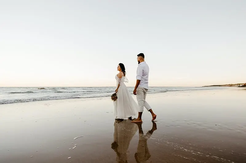 romantic newlyweds walking on the beach on sundown