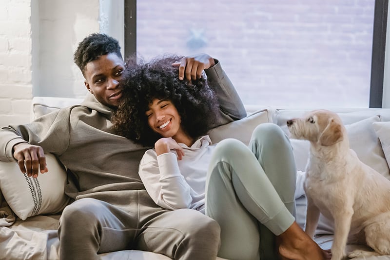 pareja sonriente acurrucada en el sofá con perro