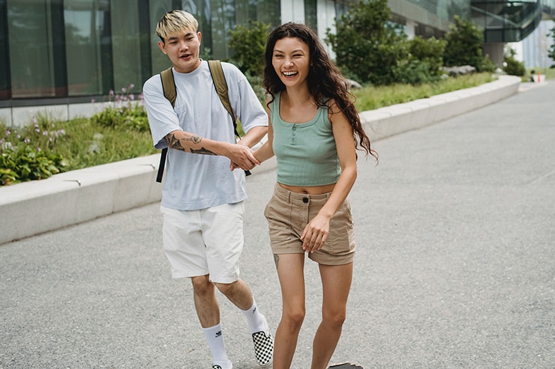 pareja sonriente cogida de la mano caminando por la acera