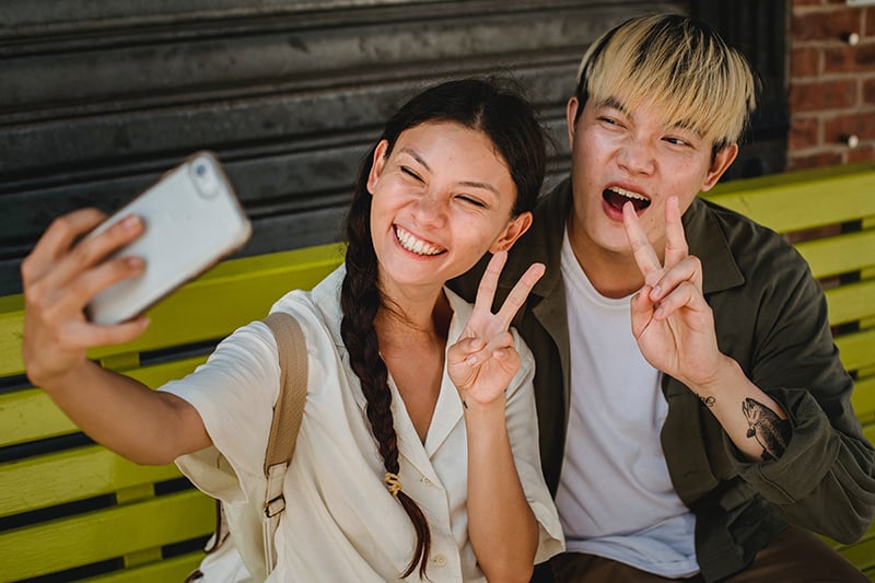 Amici sorridenti che scattano un selfie con lo smartphone e si siedono sulla panchina