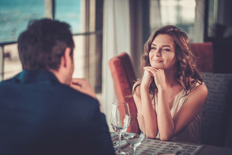 donna sorridente che ascolta attentamente un uomo seduto di fronte a lei al ristorante