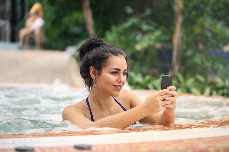 smiling woman using smartphone in jacuzzi