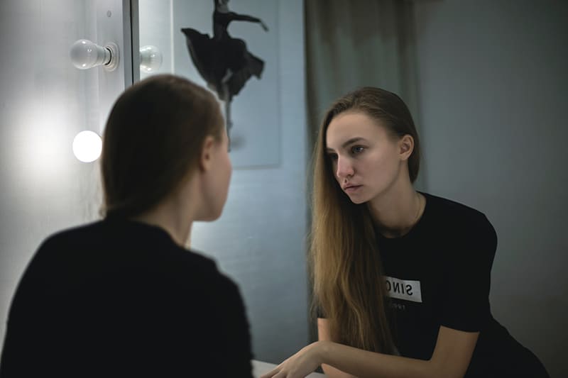 thoughtful sad woman standing in front of the mirror in the room