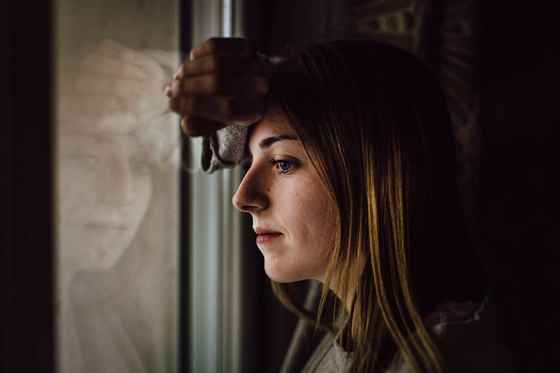 mujer pensativa apoyada en la ventana mirando al exterior