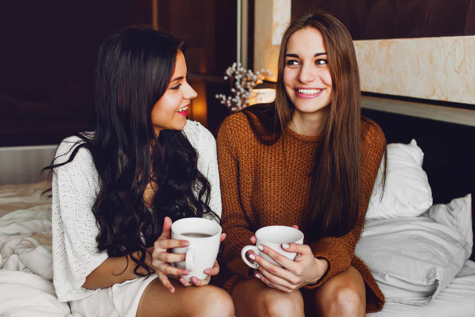 dois melhores amigos a conversar e a rir sentados na cama em casa