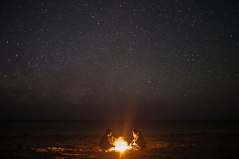 two persons sitting near bonfire on the coast at night