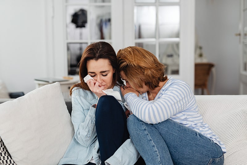 two women crying together sitting on the sofa