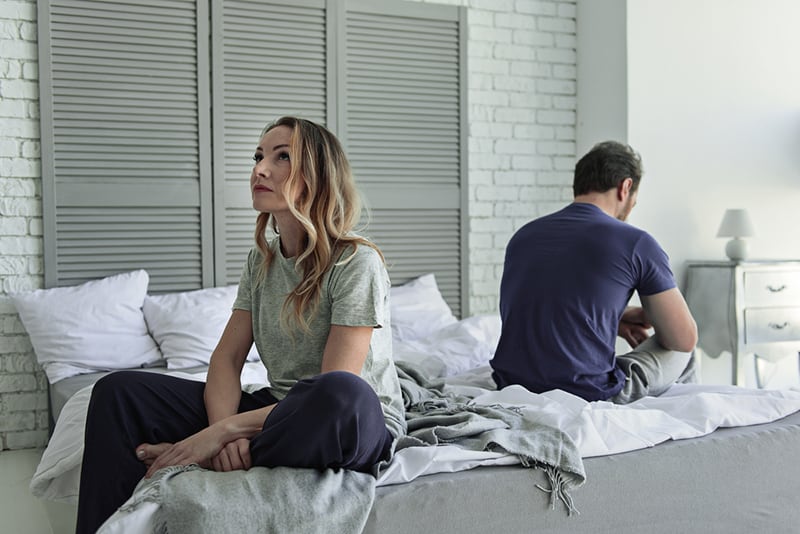 upset couple sitting on the bed turning their back to each other