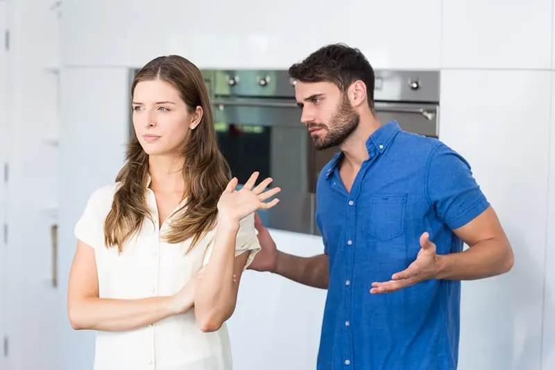 upset woman refusing to listening her husband standing beside her in the kitchen