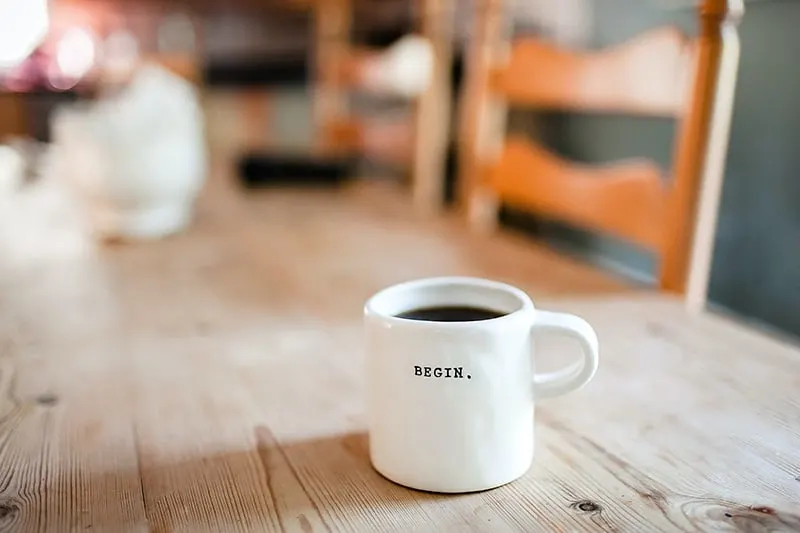 white ceramic mug with message Begin which standing on wooden table