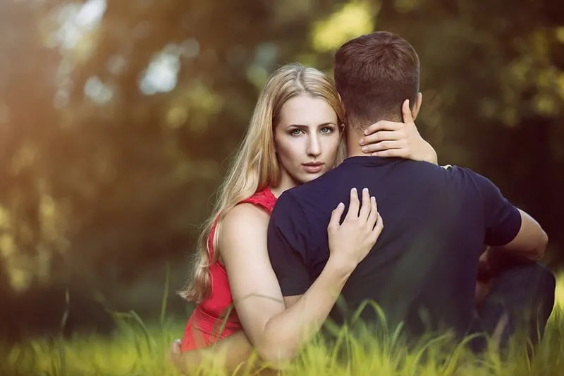 woman embracing her boyfriend while sitting in the grass field