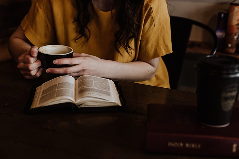 woman holding a mug while reading a bible