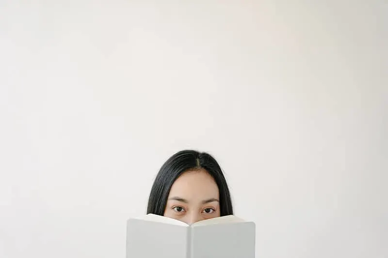 woman holding book and covering mouth with it