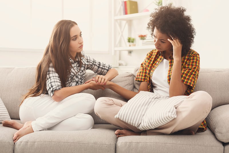 woman holding hand of her sad female friend and consoling her