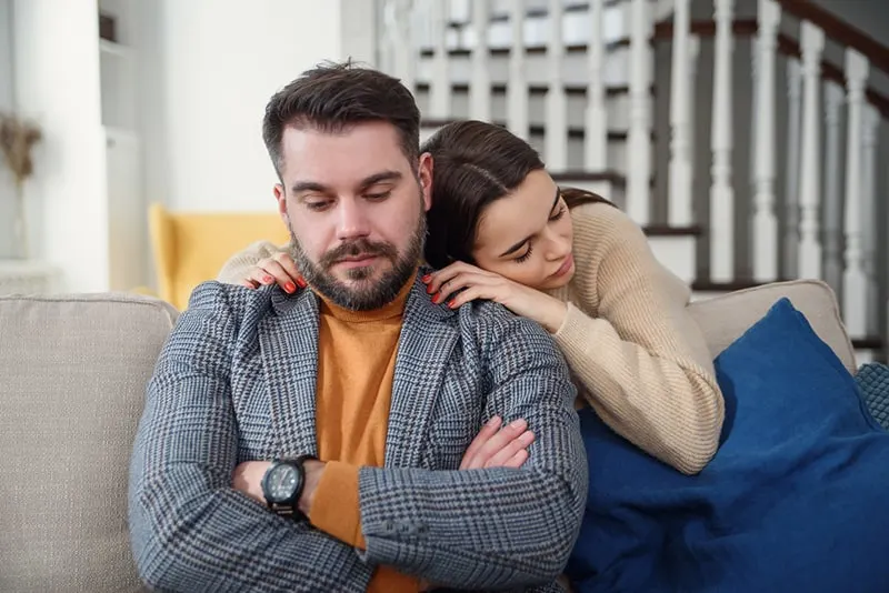 woman hugging upset boyfriend sitting on the couch