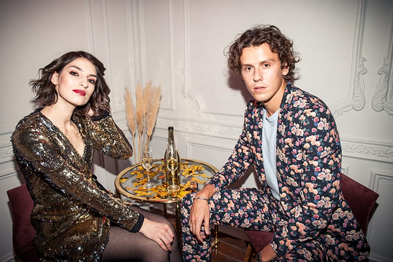 woman in shiny dress and man in floral suit sitting together by the table