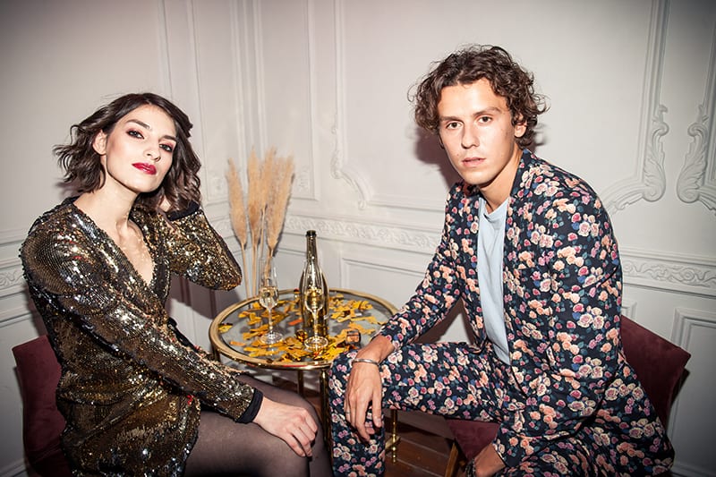 mujer con vestido brillante y hombre con traje de flores sentados juntos junto a la mesa