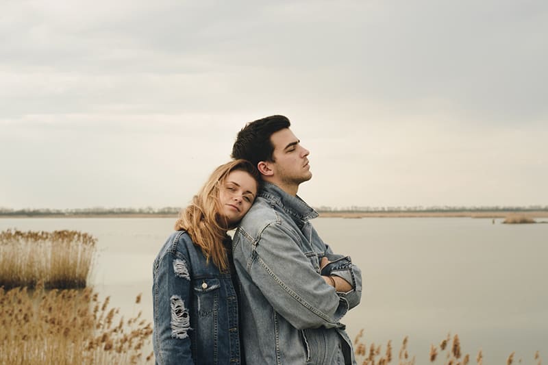 woman leaning on her boyfriend while standing near the lake