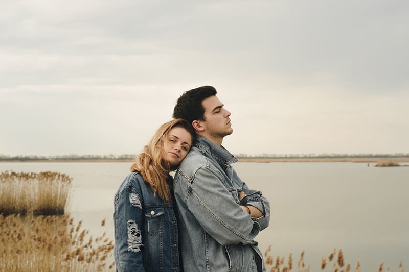 woman leaning on the back of her boyfriend while together standing near the body of water 