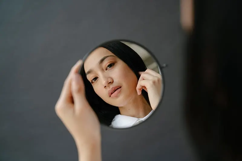woman looking at mirror holding it in her hand