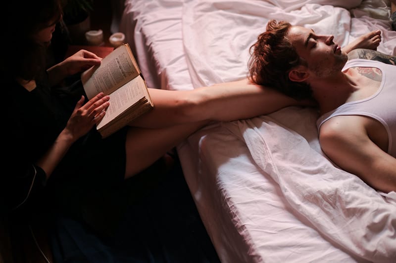 woman reading a book to her boyfriend lying on the bed
