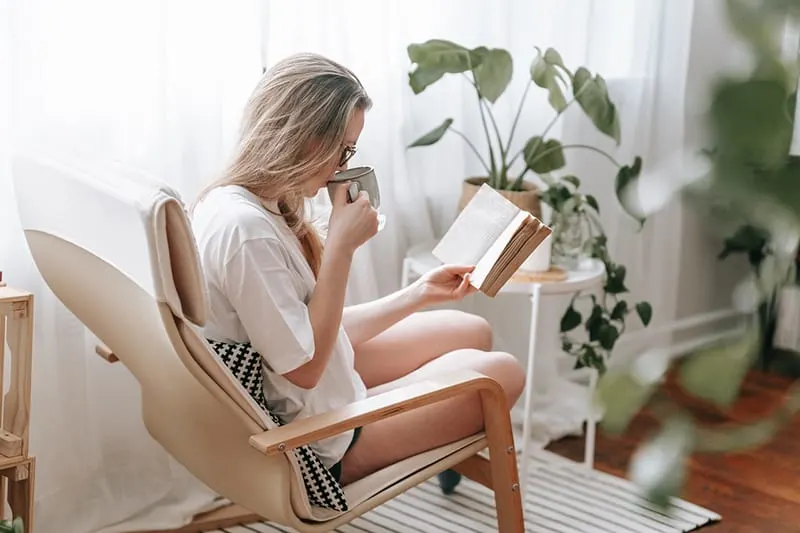 woman reading a book and drinking coffee at home