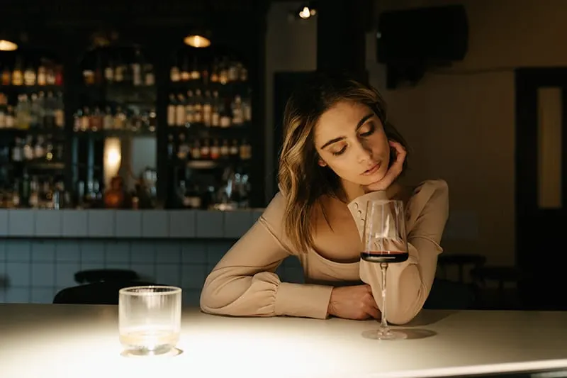 woman sitting alone at the bar and looking at glass of wine