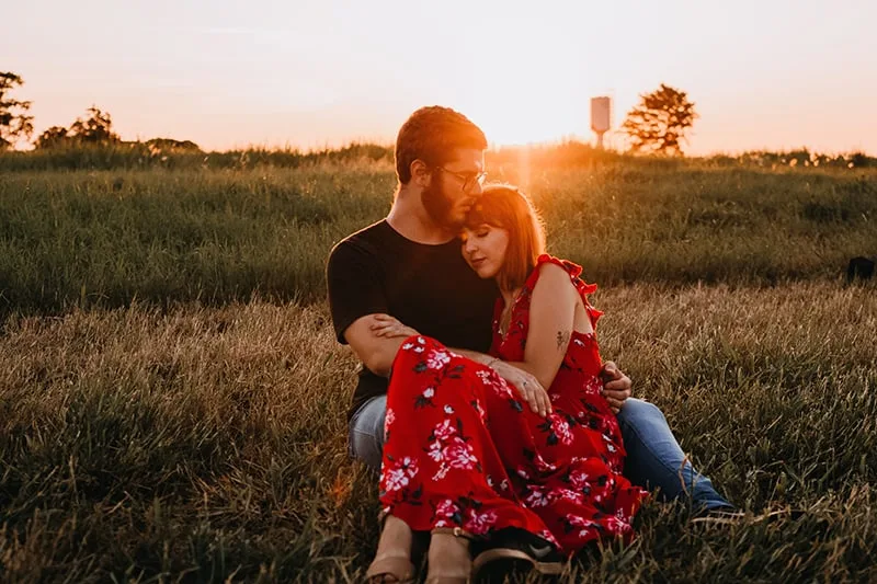 woman sitting in her boyfriend's arms in the grass field