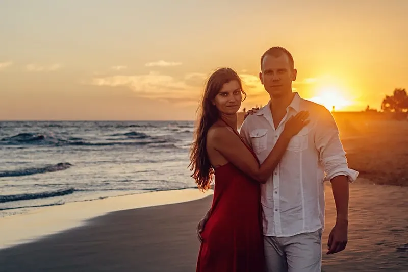 woman standing beside man on the seashore during sunset