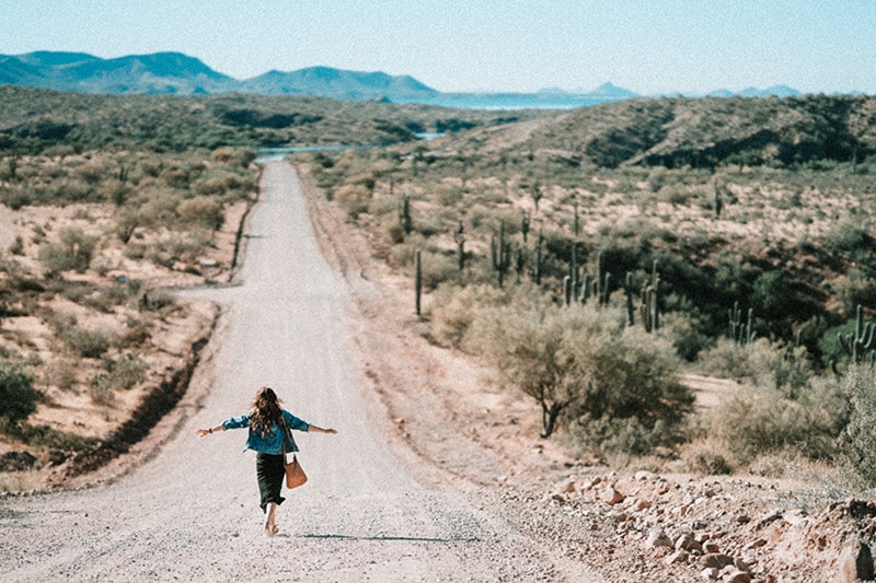 mujer caminando por un camino de tierra extendiendo los brazos