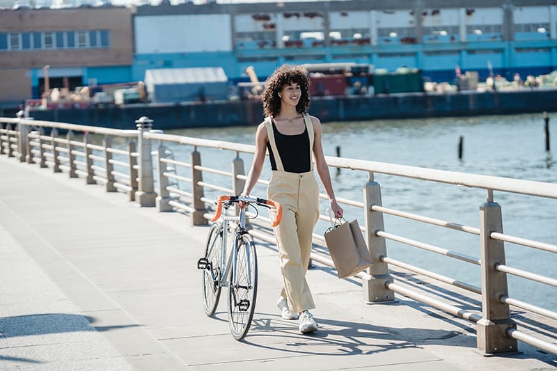 mujer caminando con bicicleta por el puente y llevando una bolsa de papel