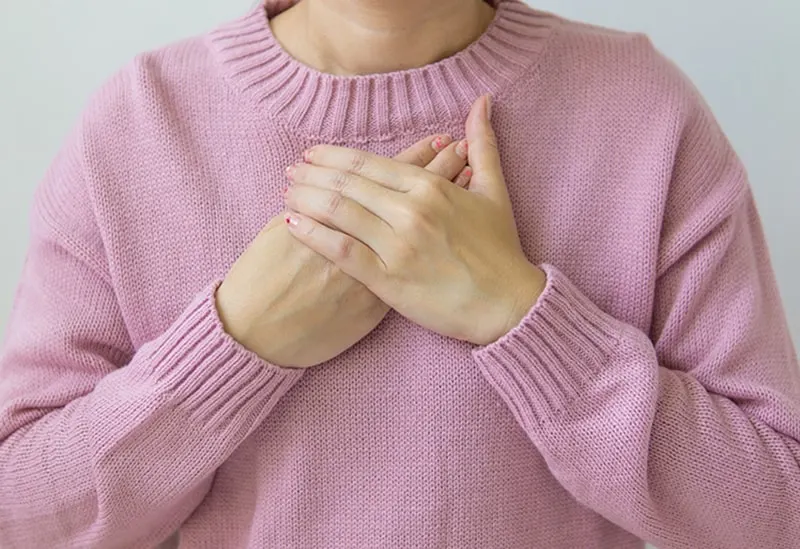 woman wearing pink sweater with hands on chests