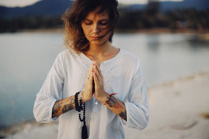 woman with closed eyes standing on the beach and praying