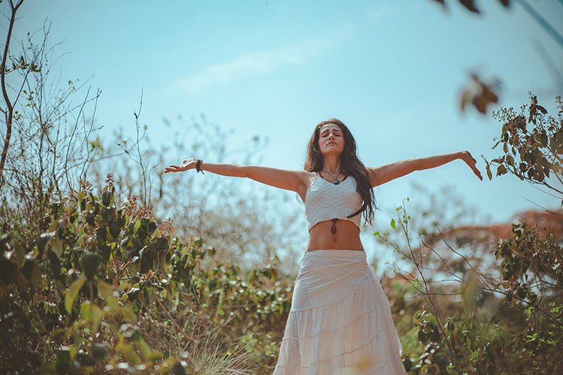 woman with closed eyes raising her arms in the field