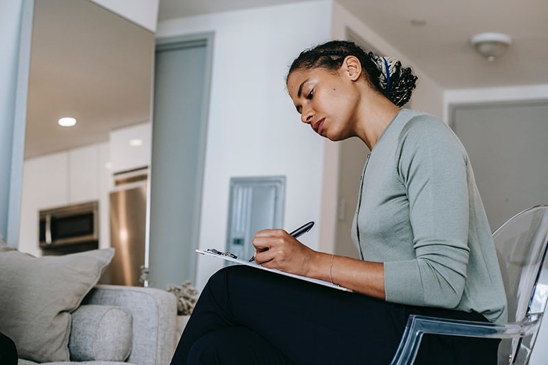 woman writing on paper and sitting in armchair