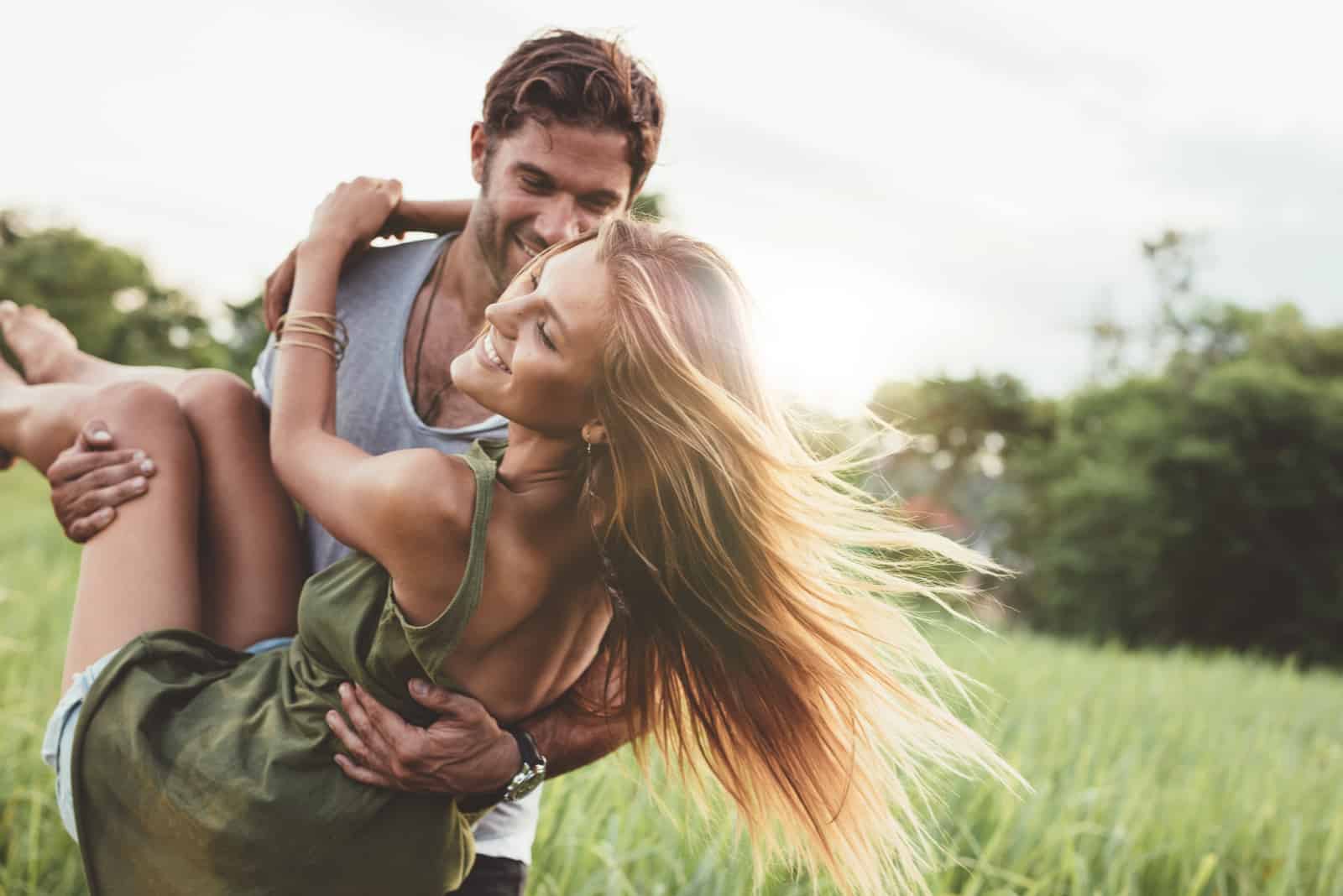 young woman being carried by her boyfriend in grass field