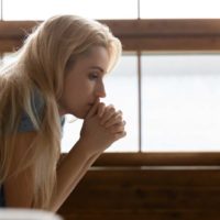 a sad blonde-haired woman sits on the bed thoughtfully