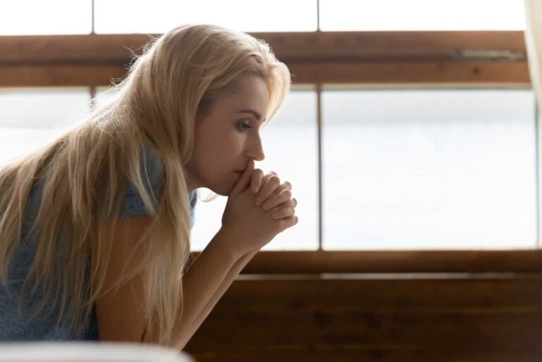 a sad blonde-haired woman sits on the bed thoughtfully