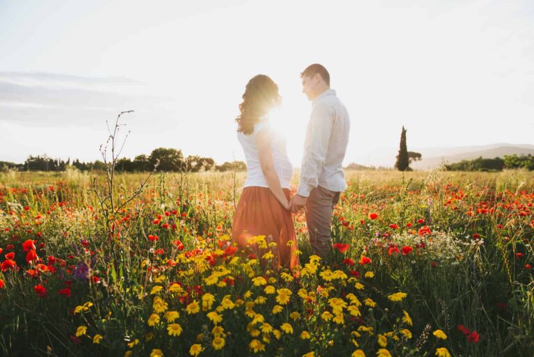 a man and a woman stand in a field of flowers and hold hands