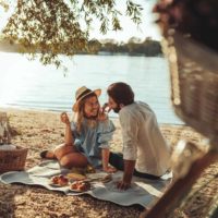 um homem e uma mulher sorridentes a tomar o pequeno-almoço na praia