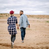 uomo e donna che si tengono per mano mentre camminano sulla sabbia