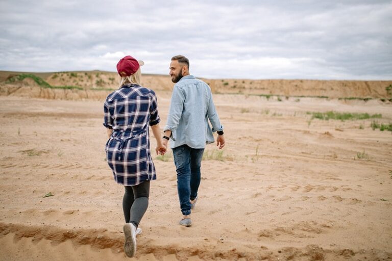 man and woman holding hands while walking on the sand
