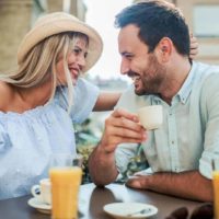 un uomo e una donna sorridenti con un cappello in testa sono seduti all'aperto in un caffè