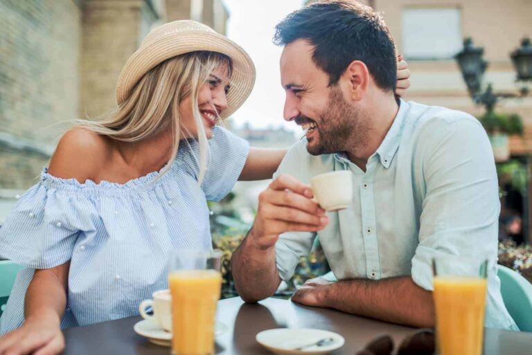 un hombre y una mujer sonrientes con un sombrero en la cabeza están sentados al aire libre en una cafetería
