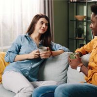 a man and a woman sit on the couch drinking coffee and talking